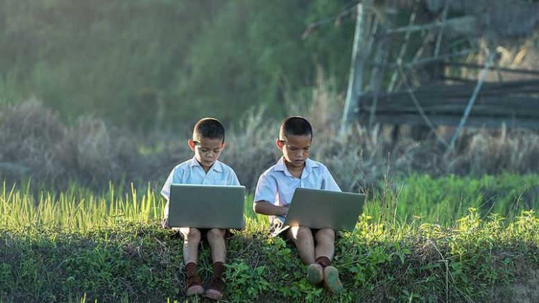 children in field on laptops